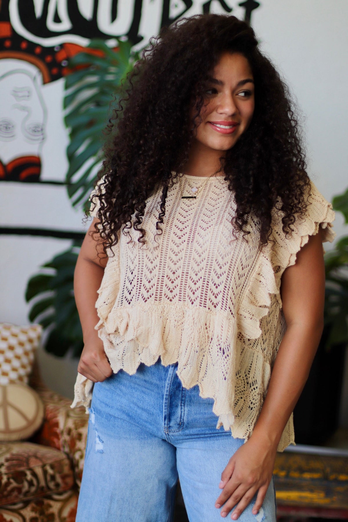 Woman wearing a beige knitted top with ruffled edges in a casual setting.
